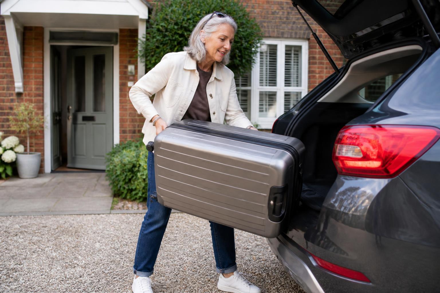 A woman in her late fifties easily lifting a heavy suitcase into the boot of her car